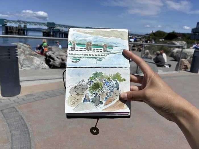 Photo of my two sketches with artists and the beach in the background